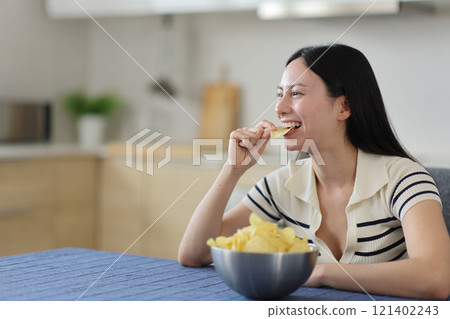 Happy asian woman eating potato chips in the kitchen 121402243