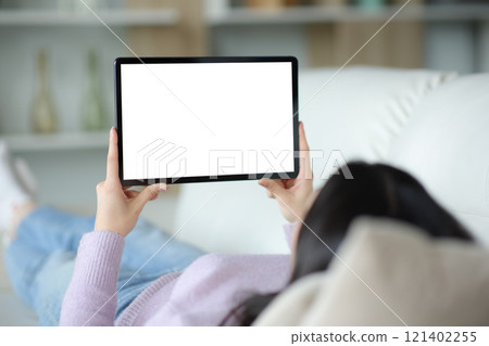 Woman on a couch using tablet showing blank screen Woman on a couch using tablet showing blank screen 121402255