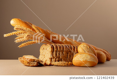 Sliced bread, baguette, and French buns with wheat ears on a beige background. Sliced bread, baguette, and French buns with wheat ears on a beige background. 121402439