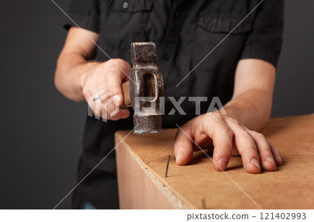 A man hammers nails into a cupboard. The back wall of the cupboard is made of thick cardboard. 121402993