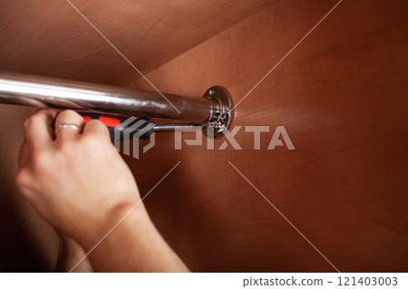 A man twists a pipe for a hanger in a closet with a screwdriver. to hang clothes. 121403003
