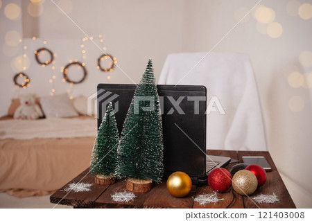 New Year's interior, decoration of the desktop and bedroom for Christmas. Boke, lights, Christmas trees, balloons, a table with a laptop with decorations. White room, wooden furniture. 121403008