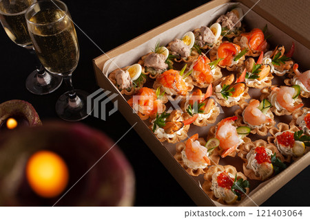 Champagne, tartlets, seafood salads. Cardboard box with food with home delivery. Gift for holiday, party, family dinner. Catering. Delicious snacks. Champagne, tartlets, seafood salads. Cardboard box with food with home delivery. Gift for holiday, party, family dinner. Catering. Delicious snacks. 121403064