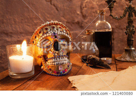 Photo zone in the studio for Halloween. Dramatic scenery for All Saints Day celebrations. The skull is decorated with beads and stones, candles, ink, crow's skull, old parchment on atable. 121403080