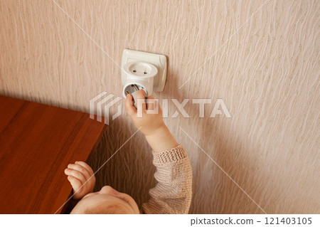 The child plays with an outlet, pulls his hands to it, sticks his fingers. The child is in danger at home. Baby fingers in the socket. 121403105