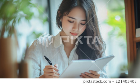 Young asian woman writing notes in notebook at home or office 121403405