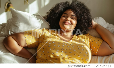Young woman relaxing in bed, enjoying sunlight and fresh air 121403445