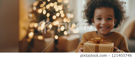 Happy child holding christmas gift in front of decorated tree 121403746
