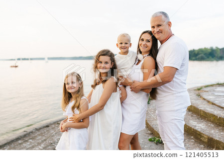 Happy family of five, including couple and three children are posing for a photo on pier by the water 121405513