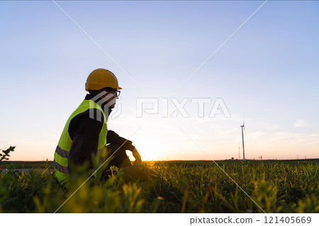 Worker sits on the grass and looks at wind turbines 121405669