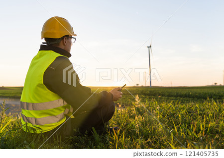 Worker sits on the grass and looks at wind turbines Worker sits on the grass and looks at wind turbines 121405735