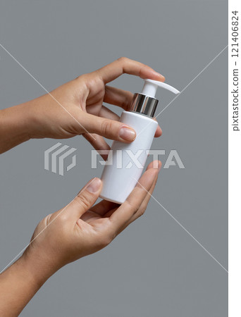 Female hands holding white cosmetic pump bottle against grey close up, mockup, copy space 121406824
