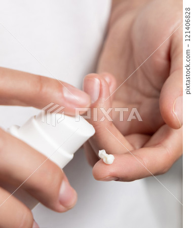 Woman squeezing hand cream on her finger and holding a cosmetic bottle in other hand, closeup Woman squeezing hand cream on her finger and holding a cosmetic bottle in other hand, closeup 121406828