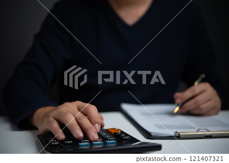 Businessperson calculating financial figures with a calculator, representing financial planning, accounting, and budgeting tasks. Businessperson calculating financial figures with a calculator, representing financial planning, accounting, and budgeting tasks. 121407321