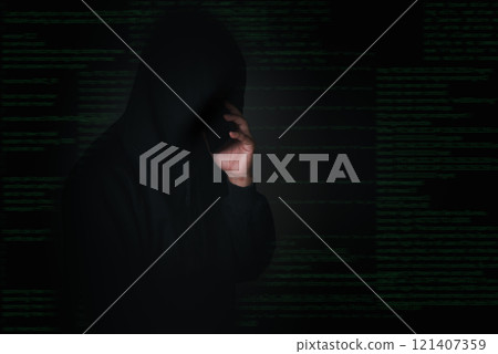 A hooded hacker is making a covert phone call, symbolizing cybercrime or identity theft planning. 121407359