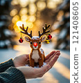 The reindeer is bathed in the golden light of morning, with a and a grand Christmas tree in the distance. 121408605