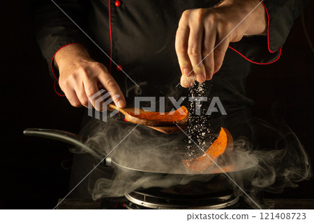 In a dimly lit kitchen, a chef expertly seasons pumpkin slices with salt, creating a fragrant mixture. Wisps of steam rise, adding a touch of culinary art to the moment In a dimly lit kitchen, a chef expertly seasons pumpkin slices with salt, creating a fragrant mixture. Wisps of steam rise, adding a touch of culinary art to the moment 121408723
