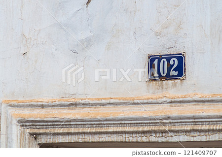 Old, slightly dirty street sign indicating the house number. The coating of the wall and the tablet, under the influence of time, became covered with cracks and rust. Concept of aging and destruction 121409707