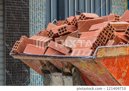 The bucket of a mini loader, which carries a fully loaded red brick down the street. An example of solving problems with low costs and with the use of ingenuity, ways to use a mini loader 121409710