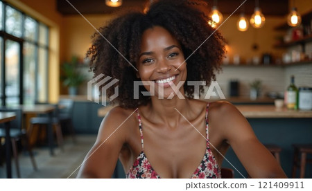 Smiling woman with natural curly hair in a cozy cafe, exuding warmth and confidence, enjoying a relaxed moment 121409911