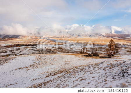 Snowy valley landscape in autumn with distant mountains and scattered trees Snowy valley landscape in autumn with distant mountains and scattered trees 121410125
