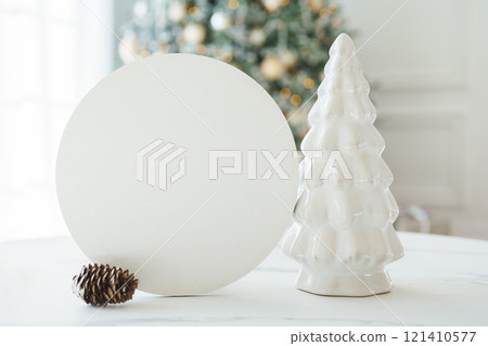 Decorative white ceramic fir tree and round empty card for text mockup on Christmas tree background 121410577