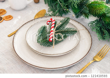 Festive dining table setting with greenery and seasonal Christmas decorations for holiday meal Festive dining table setting with greenery and seasonal Christmas decorations for holiday meal 121410593