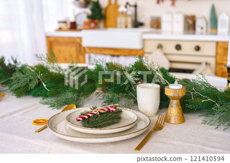 Festive dining table setting with greenery and seasonal Christmas decorations for holiday meal Festive dining table setting with greenery and seasonal Christmas decorations for holiday meal 121410594