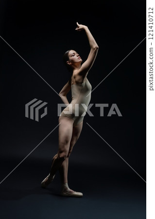 Elegant ballet dancer poses dramatically in a dark studio setting Elegant ballet dancer poses dramatically in a dark studio setting 121410712