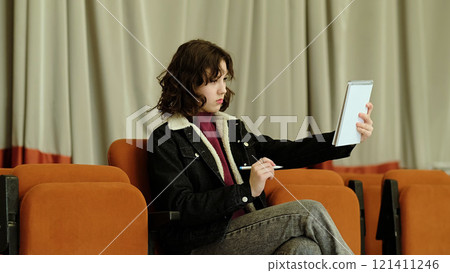 A girl with a focused yet humorous expression stretches out her notebook, symbolizing effort and creativity. The photo captures moments of playful determination and personal engagement. 121411246
