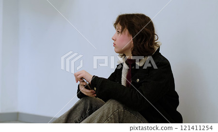 A girl with a solemn expression rests her head in her hand, seated in a minimalistic space. This photo represents feelings of loneliness, worry, or personal reflection. 121411254