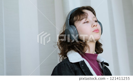 A calm young girl with headphones enjoys a quiet and reflective moment, emphasizing emotional connection and the beauty of stillness in a fast-paced world. 121411255