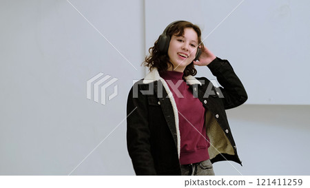 A cheerful girl with headphones sings joyfully in a minimalist setting. The scene conveys the uplifting power of music and the uninhibited expression of emotions through song. 121411259