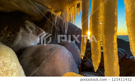 Icicles against the backdrop of the sea and large stones. Frozen wave 121411432