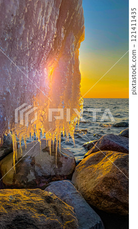 Icicles against the backdrop of the sea and large stones. Frozen wave 121411435