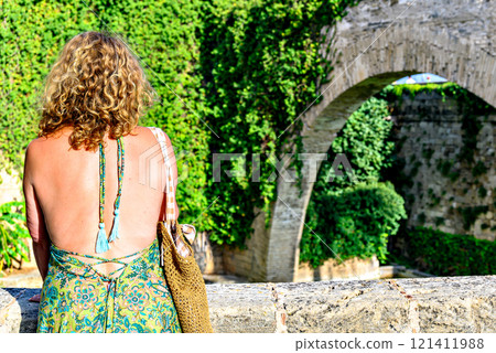 Blonde woman with curly hair looking at the swan pond of the Huerto del Rey, at the foot of the Royal Palace of Almudaina or Alcazar Real, Mallorca Blonde woman with curly hair looking at the swan pond of the Huerto del Rey, at the foot of the Royal Palace of Almudaina or Alcazar Real, Mallorca 121411988