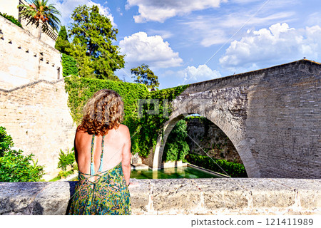 Blonde woman with curly hair looking at the swan pond of the Huerto del Rey, at the foot of the Royal Palace of Almudaina or Alcazar Real, Mallorca 121411989