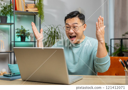 Amazed Asian man use laptop computer, receive good news message shocked by victory, celebrate win 121412071