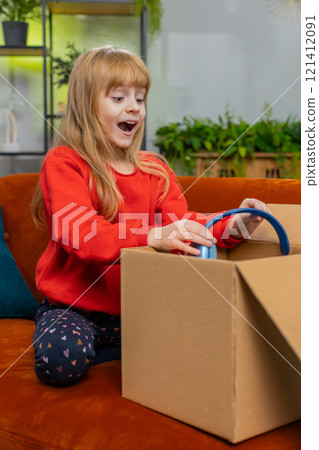 Happy child girl shopper unpacking cardboard box delivery parcel online shopping purchase at home 121412091