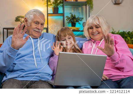 Grandfather grandmother and child granddaughter making video call online on laptop at home sofa 121412114