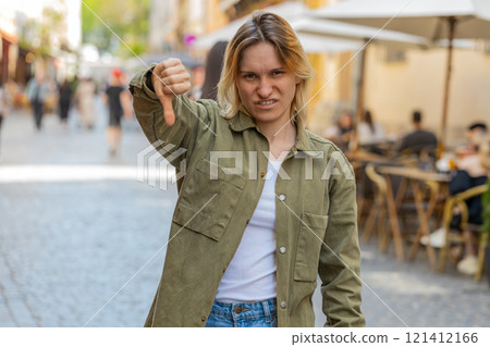 Upset young woman showing thumbs down sign disapproval, dissatisfied bad feedback on city street Upset young woman showing thumbs down sign disapproval, dissatisfied bad feedback on city street 121412166