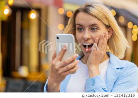 Excited happy winner woman use smartphone looking amazed at screen celebrating win good message news Excited happy winner woman use smartphone looking amazed at screen celebrating win good message news 121412319