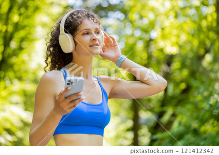 Athletic fitness sport runner woman walking, wearing headphones listening music from smartphone 121412342