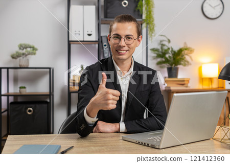 Smiling young Caucasian businessman freelancer showing double thumbs up sitting at home office desk Smiling young Caucasian businessman freelancer showing double thumbs up sitting at home office desk 121412360