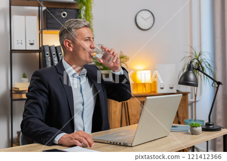 Handsome young freelancer using laptop and drinking glass of water sitting at home office desk Handsome young freelancer using laptop and drinking glass of water sitting at home office desk 121412366