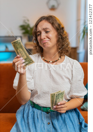 Upset young woman sitting on sofa counting money, having not enough, worried about finances, debts Upset young woman sitting on sofa counting money, having not enough, worried about finances, debts 121412377