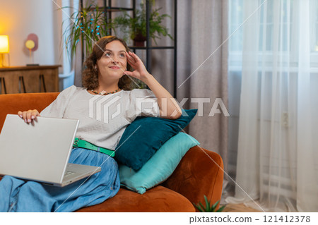 Happy Caucasian woman sitting on couch closing laptop after finishing work in living room at home Happy Caucasian woman sitting on couch closing laptop after finishing work in living room at home 121412378
