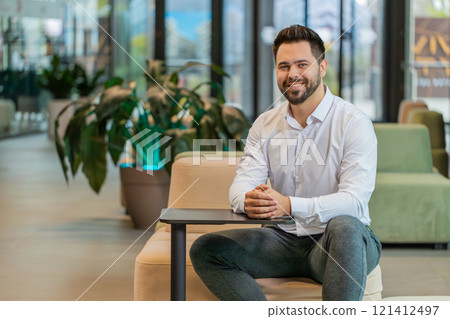 Portrait of smiling young businessman looking at camera sitting in hotel lobby Portrait of smiling young businessman looking at camera sitting in hotel lobby 121412497