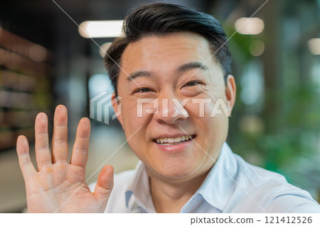 Portrait of happy Chinese businessman looking at camera and waves hand hello in office hotel lobby Portrait of happy Chinese businessman looking at camera and waves hand hello in office hotel lobby 121412526
