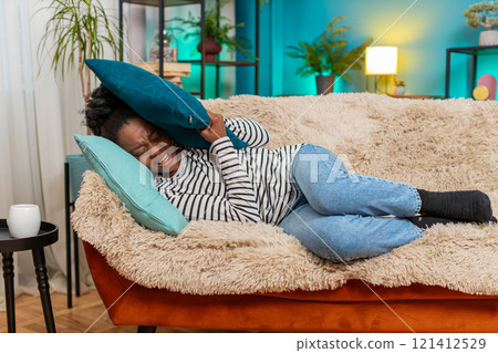 African American woman lying on sofa closing eyes covering face with pillow feeling migraine pain African American woman lying on sofa closing eyes covering face with pillow feeling migraine pain 121412529